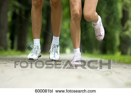 Stock Image - close-up of legs of two young woman jogging through park. Fotosearch