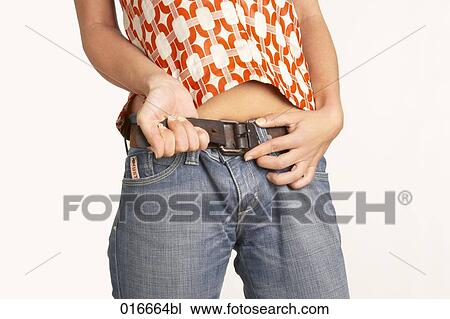 Stock Image - close-up of young woman pulling belt of her jeans. Fotosearch