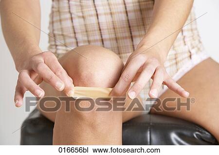 Stock Image - detail of young woman putting band-aid on her knee. Fotosearch