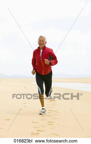 Stock Image - full body portrait of mature man jogging on beach. Fotosearch