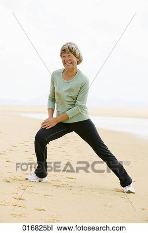 Stock Image - full body portrait of mature woman exercising on beach. Fotosearch