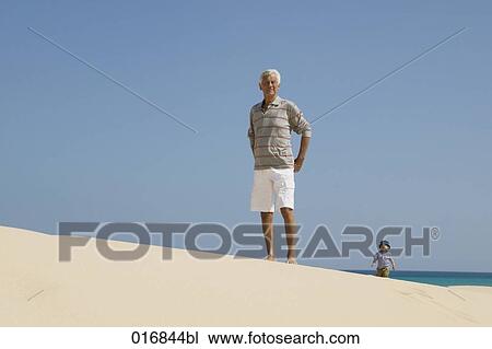 Stock Image - full boy portrait of mature man on beach with toddler in background. Fotosearch