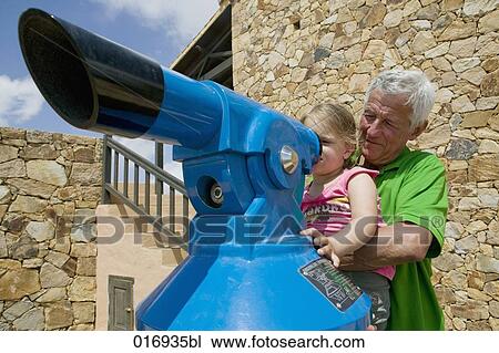 Stock Image - grandfather helöping little girl to look through binocular. Fotosearch