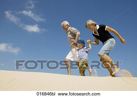 Stock Image - grandparents walking on beach with toddler. Fotosearch