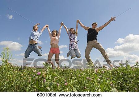Stock Image - group of four friends jumping in summer meadow. Fotosearch