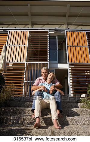 Stock Image - happy couple sitting in front of home. Fotosearch