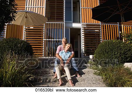 Stock Image - happy couple sitting in front of home. Fotosearch
