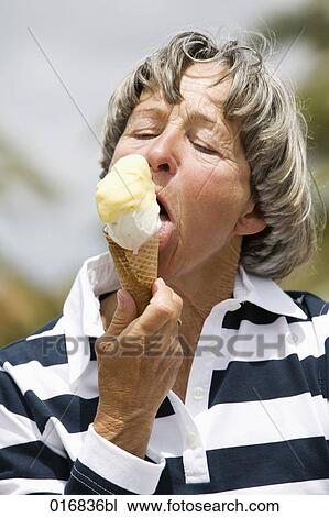Stock Image - headshot of mature woman licking ice cream. Fotosearch