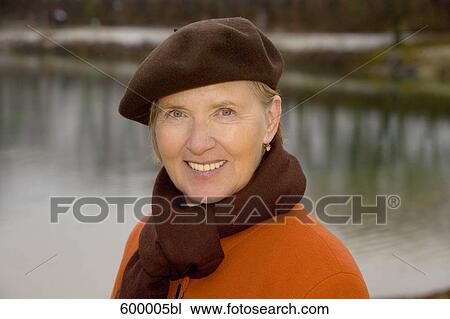 Stock Image - headshot of mature woman wearing brown beret standing at lake in park. Fotosearch