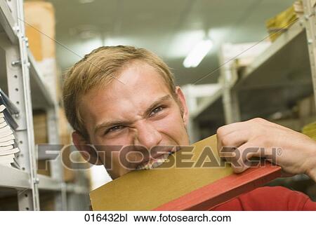 Stock Image - headshot of young male student biting into textbook. Fotosearch