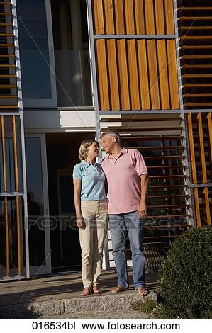 Stock Image - mature couple in front of home tenderly looking at each other. Fotosearch