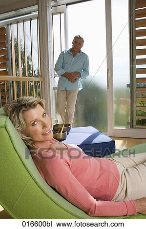 Stock Image - mature couple in living at home woman lying on chair. Fotosearch