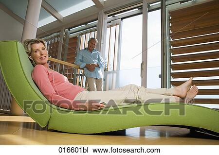 Stock Image - mature couple in living at home woman lying on chair listening to music. Fotosearch