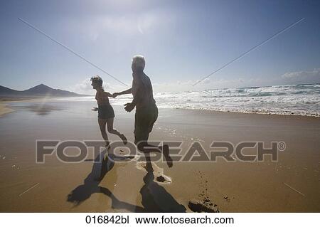 mature couple in swimwear running along beach hand in hand View Large Photo Image Stock Image - mature couple in swimwear running along beach hand in hand. Fotosearch
