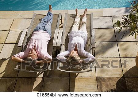 Stock Image - mature couple lying on sun loungers near swimming pool. Fotosearch
