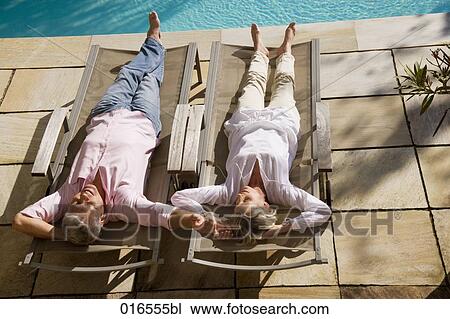 Stock Image - mature couple lying on sun loungers near swimming pool. Fotosearch