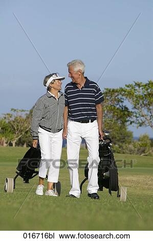Stock Image - mature couple pulling golf bags over golf course. Fotosearch