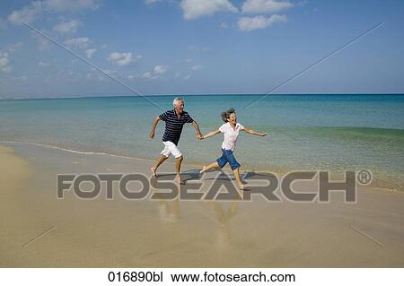 mature couple running along beach hand in hand View Large Photo Image Stock Image - mature couple running along beach hand in hand. Fotosearch