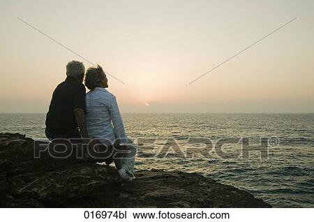 mature couple sitting on rock watching sunset over sea View Large Photo Image Stock Image - mature couple sitting on rock watching sunset over sea. Fotosearch