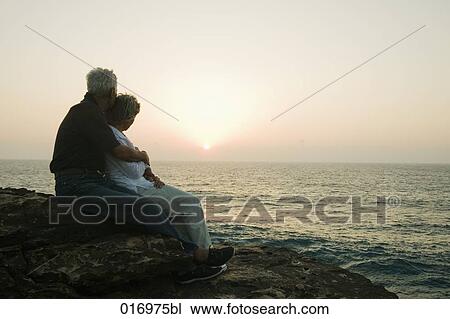 mature couple sitting on rock watching sunset over sea View Large Photo Image Stock Image - mature couple sitting on rock watching sunset over sea. Fotosearch