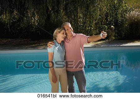 mature couple taking self-portrait with digital camera in front of swimming pool View Large Photo Image Stock Image - mature couple taking self-portrait with digital camera in front of swimming pool. Fotosearch