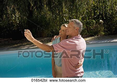 mature couple taking self-portrait with digital camera in front of swimming pool View Large Photo Image Stock Image - mature couple taking self-portrait with digital camera in front of swimming pool. Fotosearch