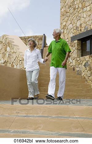 Stock Image - mature couple walking down stairs hand in hand. Fotosearch