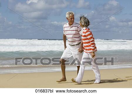 Stock Image - mature couple walking hand in hand along beach. Fotosearch