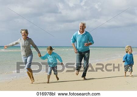 Stock Image - mature couple with their grandchildren having a walk along the beach. Fotosearch