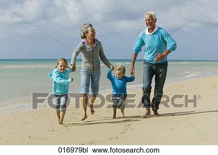 Stock Image - mature couple with their grandchildren having a walk along the beach. Fotosearch