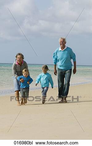 Stock Image - mature couple with their grandchildren having a walk along the beach. Fotosearch