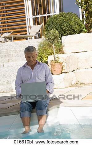 mature man sitting at swimming pool and working with laptop computer View Large Photo Image Stock Image - mature man sitting at swimming pool and working with laptop computer. Fotosearch