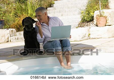 mature man sitting at swimming pool with dog and working with laptop computer View Large Photo Image Stock Image - mature man sitting at swimming pool with dog and working with laptop computer. Fotosearch