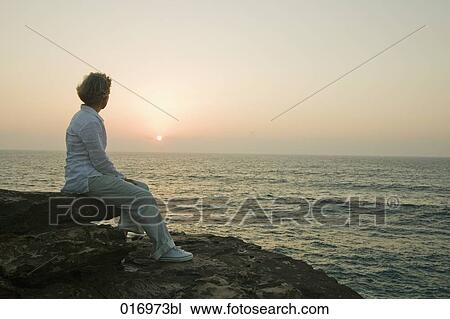 mature woman sitting on rock watching sunset over sea View Large Photo Image Stock Image - mature woman sitting on rock watching sunset over sea. Fotosearch