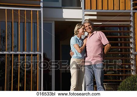 Stock Image - portrait of mature couple standing in front of home. Fotosearch