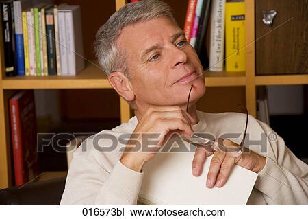 Stock Image - portrait of mature man holding spectacles und book. Fotosearch