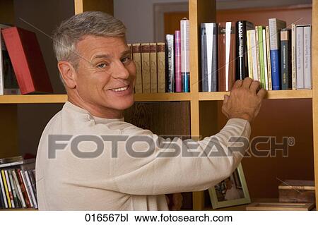 Stock Image - portrait of mature man taking book from shelf. Fotosearch