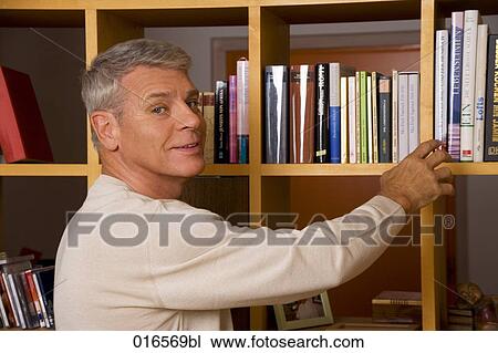 Stock Image - portrait of mature man taking book from shelf. Fotosearch