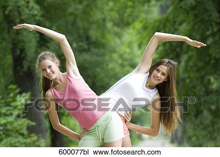 Stock Image - portrait of two young women doing stretching exercises in park. Fotosearch