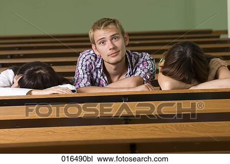 Stock Image - portrait of young student in lecture hall while all others are sleeping. Fotosearch