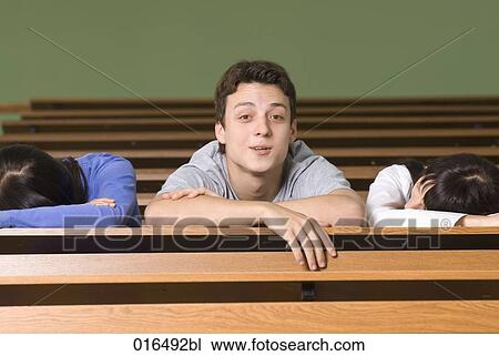 Stock Image - portrait of young student in lecture hall while all others are sleeping. Fotosearch