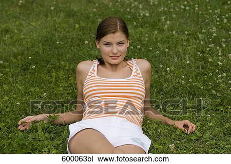 Stock Image - portrait of young woman lying on lawn in park. Fotosearch