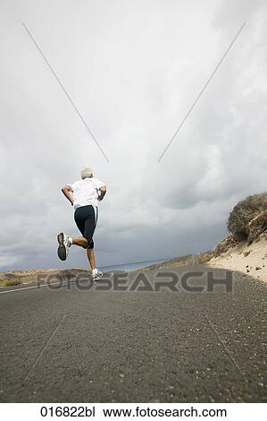 rear view of mature man jogging along empty road View Large Photo Image Stock Image - rear view of mature man jogging along empty road. Fotosearch