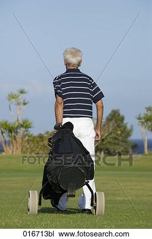 Stock Image - rear view of mature man pulling golf bag over golf course. Fotosearch