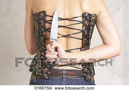 Stock Image - rear view of young woman hiding big knife behind her back. Fotosearch