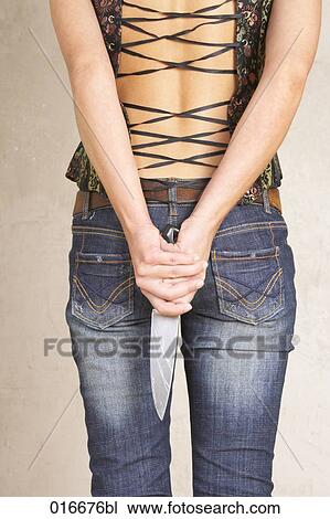 Stock Image - rear view of young woman hiding big knife behind her back. Fotosearch