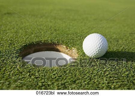 Stock Image - still life of golf ball by hole on putting green. Fotosearch