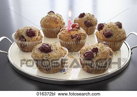 Stock Image - still life of seven cherry muffins on tray one decorated with burning candle. Fotosearch