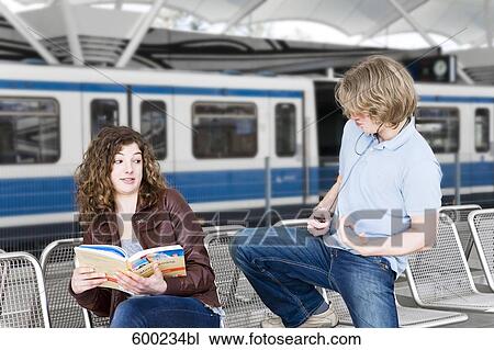Stock Image - teenage boy playing air guitar in front of girl at underground station. Fotosearch