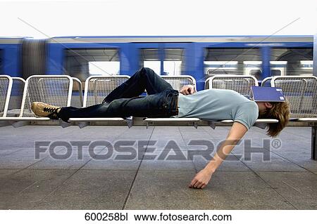Stock Image - teenage boy sleeping on bench at station. Fotosearch